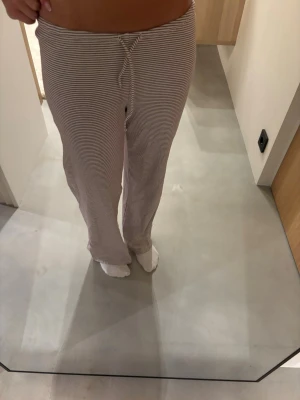 Randiga loungebyxor  - Mysiga loungebyxor med tunna beige och vita ränder. Byxorna har rak passform, resår i midjan och dragsko för justerbar komfort🌸
