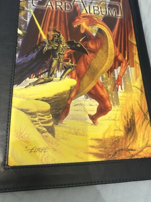Kortalbum med fantasyomslag - Snyggt samlaralbum för kort med ett färgstarkt fantasyomslag där en riddare slåss mot en röd drake. Albumet har svarta kanter och plastfickor för att förvara samlarkort, exempelvis Pokémonkort. Omslaget är illustrerat av Elmore och ger albumet en unik look.