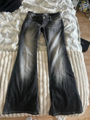 Grå bootcut jeans blaze - Säljer ett par svarta bootcut jeans med ljusare tvätt framtill. Jeansen har klassisk femficksmodell, låg midja och vida ben. Perfekta för dig som gillar retrostil och vill ha ett par jeans som sticker ut. Strl S short, blaze