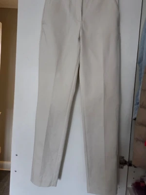 ENDAST PROVADE  1 G Beiga / Creme färgade  kostymbyxor från H&M stl 34  - Snygga beiga kostymbyxor från H&M med klassisk rak passform och pressveck. Materialet är bomull och polyester, vilket ger en skön och stilren känsla. Perfekta för dig som vill ha ett clean och elegant look. Innerbenslängd ca 69 cm , materialet är 57 % bomull 40 % polyester och 3 % elastan 