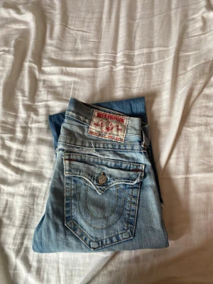 True Religion ljusblå  jeans - Säljer ett par ljusblå jeans från True Religion med  klassiska kontrastsömmar. Row 31, seat 33. Säljer eftersom jag byt still och inte använder dom längre och för att jag är desperat för pengar till sommaren. Jeansen har en stor ficka bak med lock och knapp samt en tydlig logga på bakfickan. Perfekta för dig som gillar streetwear och avslappnad stil.