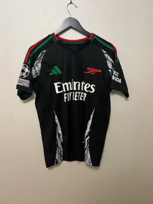 Arsenal Matchtröja  - Hej, säljer en Arsenal tröja med Saliba på ryggen och Champions League märke på ärmen. Tröjan är i väldigt bra skick. Har ett liten defekt vid Champions league loggan där märket tappat lite lim men det är inget man tänker på