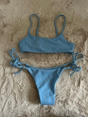 Ljusblå  bikini  - Trendig ljusblå bikini med ribbad struktur och smala axelband. Bikinin har knyt i sidorna för justerbar passform, aldrig använd, storlek xs