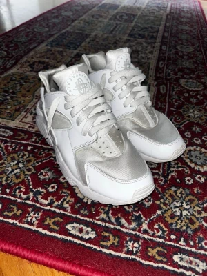 Nike Huarache Triple White - Säljer ett par Nike Air Huarache sneakers i vitt med inslag av ljusgrått. Skorna har en chunky design, klassiska snörningar och detaljer i både läder och mesh. Perfekta för dig som vill ha en clean och sportig look.