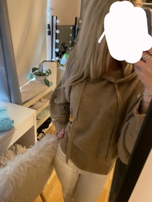 Beige stickad hoodie med huva - Mysig beige stickad hoodie med huva och dragsko. Tröjan har långa ärmar och breda ribbade muddar vid ärmslut och nederkant. Perfekt för en avslappnad och trendig look. Materialet är mjukt och skönt. Jätte mysig tröja som man kan vara både bekväm och snygg i. 