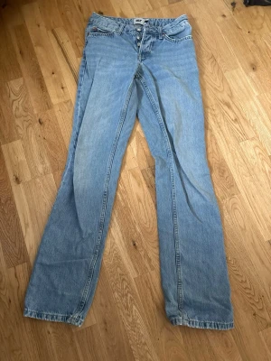 Ljusblå raka jeans från 157 - Säljer ett par ljusblå jeans från 157 med raka ben och låg midja. Klassisk femficksmodell med knappgylf och bälteshällor. Jeansen är gjorda i denim och har en avslappnad passform som passar perfekt till en casual stil.