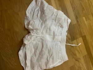 Vita linneshorts med dragsko - Säljer ett par vita shorts i luftigt linne med elastisk midja och dragsko. Shortsen har en avslappnad passform och en bakficka. Perfekta för varma dagar och enkel att matcha med olika toppar.