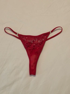 Röd spetsstringtrosa  - Snygg röd stringtrosa med tunna sidoband och dekorativ spets framtill. Perfekt för dig som gillar en sexig och stilren look.