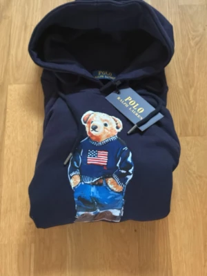 Mörkblå Polo Ralph Lauren Bear Hoodie M - Storlek M helt ny med original prislapp kvar så skicket är i topklass bara testad på en gång men inte mer än det hör av er vid funderingar eller frågor pris kan diskuteras vid snabb affär