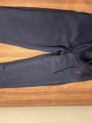 Svarta mjukisbyxor Polo Ralph Lauren - Snygga svarta mjukisbyxor från Polo Ralph Lauren med dragsko i midjan och den klassiska röda loggan broderad på benet. Tillverkade i mjukt material som känns skönt mot huden. Perfekta för en avslappnad och trendig look. Storlek S. Skön, mysiga och puffiga. 
