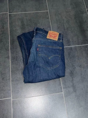 Levi's blå 527 bootcut jeans - Klassiska blå jeans från Levi's med raka ben och femficksmodell. Jeansen har en mörk tvätt med lätt slitning framtill och den ikoniska läderpatchen bak i midjan. Tillverkade i slitstark denim med snygga kontrastsömmar.