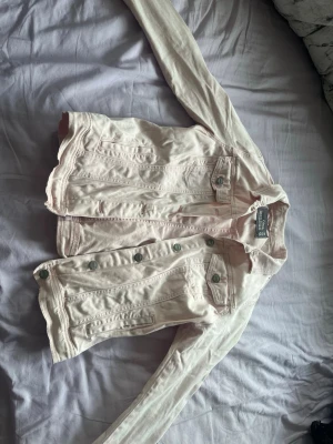 Ljusrosa jeansjacka från Gina Tricot - Snygg ljusrosa jeansjacka från Gina Tricot med klassisk knappstängning framtill och två bröstfickor med lock och knapp. Jackan har långa ärmar och en rak passform som ger en avslappnad look. Perfekt att slänga över en t-shirt för en cool vibe.