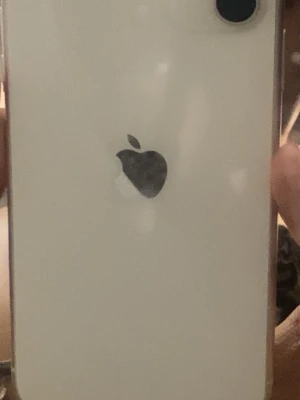 Vit iPhone med Apple-logga - Säljer en vit iPhone med klassisk Apple-logga på baksidan. Telefonen har rundade hörn och en enkel, stilren design. Kameran sitter i det övre vänstra hörnet och baksidan är i glas. Perfekt för dig som gillar snygg och modern teknik. Den är jätte ny knappast använt. Säljer telefonen för jag tycker inte om färgen.