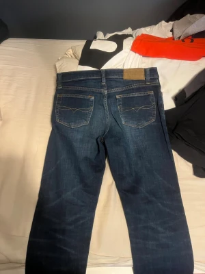 Mörkblå raka jeans från Polo Ralph Lauren - Säljer ett par mörkblå jeans från Polo Ralph Lauren med klassisk rak passform. Jeansen har fem fickor, kontrastsömmar och en läderpatch bak i midjan. Tillverkade i slitstark denim med snygga tvättade detaljer.