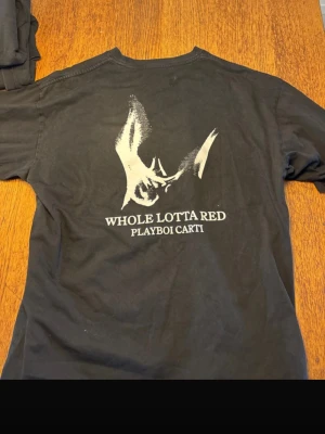 Playboi Carti Whole Lotta Red t-shirt - Säljer en svart t-shirt från Playboi Carti med trycket 'Whole Lotta Red' på ryggen och ett stort grafiskt motiv i vitt både fram och bak. T-shirten har rund hals och korta ärmar, perfekt för dig som gillar streetwear och vill sticka ut.