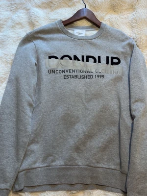 Grå sweatshirt från Dondup - Snygg grå sweatshirt från Dondup med tryckt text 'UNCONVENTIONAL CLOTHING ESTABLISHED 1999' på bröstet. Klassisk rund halsringning och ribbade muddar vid ärmslut och nederkant. 