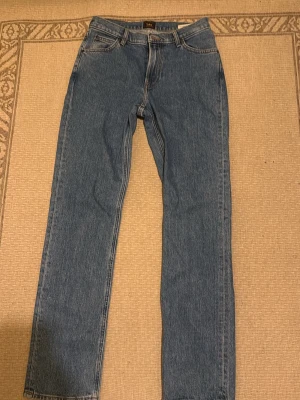 Blå raka jeans från Lee - Klassiska blå jeans från Lee med rak passform och fem fickor. Jeansen har normal midja, dragkedjegylf och Lee-lapp bak i midjan. Tillverkade i slitstark denim som ger en tidlös look. Perfekta till sneakers eller boots.