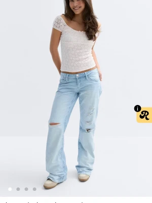 Ljusblå slitna bootcut jeans - Säljer ett par ljusblå bootcut jeans med slitningar och hål på benen. Jeansen har klassisk femficksmodell och låg midja. Perfekta för en avslappnad och trendig look. Materialet är denim i bomull.