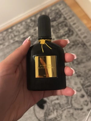 Tom Ford Black Orchid 30 ml parfym - Lyxig parfym från Tom Ford, Black Orchid, i en elegant svart flaska med gulddetaljer och räfflad yta. Flaskan rymmer 30 ml och har en exklusiv design med guldetikett och dekorativt band runt halsen. Perfekt för dig som gillar unika och djupa dofter.