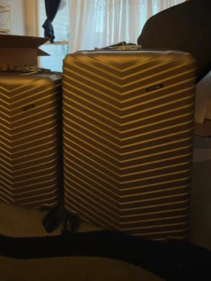 Set med två guldiga resväskor alkano - Säljer ett set med två resväskor från alkanoi metallic guld. Väskorna har ett modernt, randigt mönster i V-form och är tillverkade i hårdplast. Båda har fyra hjul för enkel manövrering och draghandtag upptill. Perfekta för resor när du vill sticka ut.