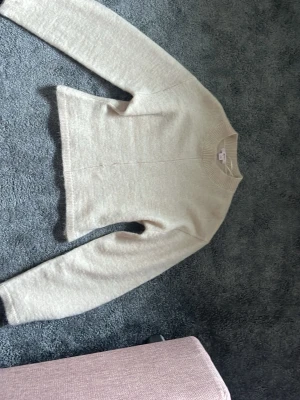 Beige stickad tröja med rund hals - En stilren beige stickad tröja med rund halsringning och långa ärmar. Tröjan har en rak passform och ribbstickade detaljer vid halsen. Perfekt att matcha med jeans eller kjol för en enkel och snygg look.