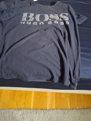 Blå Hugo Boss t-shirt - Blå t-shirt från Hugo Boss med stort, vitt logotryck på bröstet. Klassisk rund halsringning och korta ärmar. Tillverkad i mjuk bomull för en bekväm känsla. Perfekt för en avslappnad och stilren look.