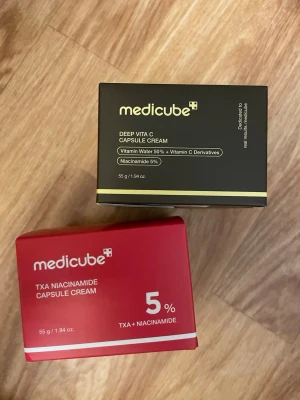 Medicube kapselkrämer 2-pack, 2 för 1 - Säljer två kapselkrämer från Medicube, båda är oöppnade och förseglade fortfarande: Deep Vita C Capsule Cream i svart förpackning med vitamin C och niacinamid, samt TXA Niacinamide Capsule Cream i röd förpackning med 5% TXA och niacinamid. Båda innehåller 55 g och är perfekta för hudvård.