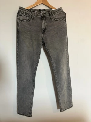 Grå tvättade jeans från Jack&jones  - Snygga grå tvättade jeans från jack&jones med raka ben. Jeansen har normal. Materialet är mjukt denim i bomull vilket gör dom väldigt komfortabla.                                  Byxorna är ALDRIG andvända.