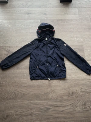 Mörkblå vindjacka från Moncler - HELT NY! 💣Snygg mörkblå vindjacka från Moncler med huva och dragkedja framtill. Qr kod och blipp funktion fungerar som den ska ✅ storlek 2 vilket motsvarar M och lite S