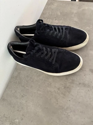 Svarta mockasneakers med vit sula - Stilrena svarta sneakers i mocka med klassisk låg profil och vita gummisulor. Skorna har svarta skosnören och en enkel, tidlös design som passar till det mesta. Perfekta för dig som gillar en clean och avslappnad look.