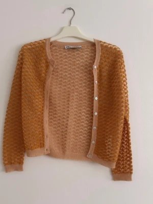 Persikofärgad transparent kofta från Zara - Säljer en persikofärgad transparent kofta från Zara med rund halsringning och långa ärmar. Koftan har ett fint strukturmönster, ribbade muddar och knäppning framtill med vita knappar. Perfekt för lager på lager och en trendig look.