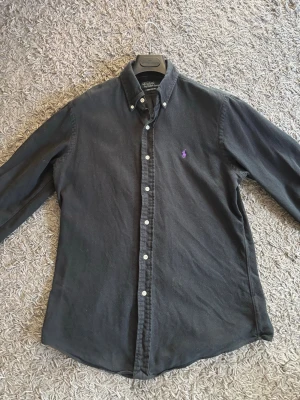 Svart Skjorta, Polo Ralph Lauren - Klassisk svart skjorta från Polo Ralph Lauren med lila broderad logga på bröstet.  Storlek M - Custom Fit 
