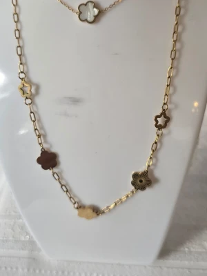 Guldfärgat halsband med armband blommor - Snyggt halsband i guldfärgad stainless steel med flera blomformade hängen i olika färger och utföranden. Kedjan har en modern, länkad design och blommorna är både fyllda och öppna, vissa med pärlemorskimrande yta. Perfekt accessoar för att lyfta din outfit.