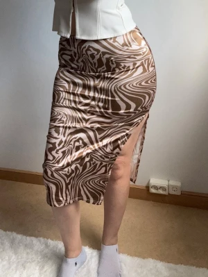 Brun zebramönstrad kjol med slits - Säljer en brun och beige zebramönstrad långkjol med hög slits på sidan. Kjolen har en tight passform och är gjord i ett mjukt, stretchigt material som känns skönt mot huden. Perfekt för dig som vill sticka ut med ett coolt mönster.