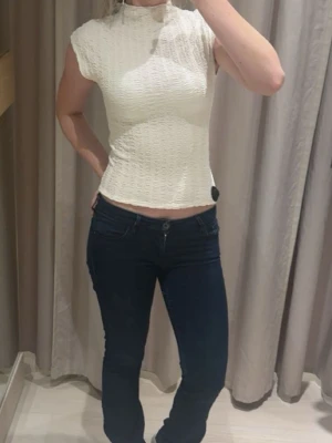 Vit ribbad croppad topp - Säljer en vit croppad topp med ribbad struktur och hög hals. Från H&M. Aldrig använd. Toppen är ärmlös och har en tight passform som framhäver figuren. Perfekt att styla med jeans eller kjol för en trendig look. Skriv för fler bilder!!💕