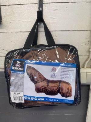 Brunt eksemtäcke - häst OneHorse - Säljer ett brunt eksemtäcke från OneHorse, perfekt för att skydda hästen mot insekter och irritation. Täcket är tillverkat i ett lätt och slitstarkt material och kommer i en praktisk förvaringsväska med handtag. Storlek 115 cm. Täcket är oanvänt och endast provat, men passade inte.
