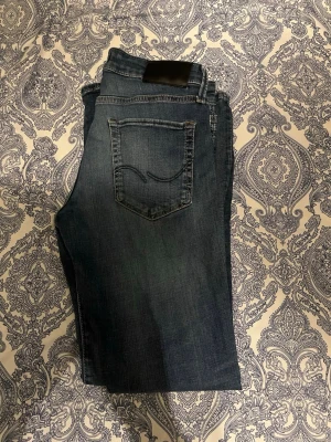 Mörkblå raka jeans från Jack & Jones - Säljer ett par mörkblå jeans från 7 For All Mankind med raka ben och klassisk femficksdesign. Jeansen har snygga slitningar och en diskret logga på bakfickan. Tillverkade i mjuk denim med lite stretch för extra komfort.
