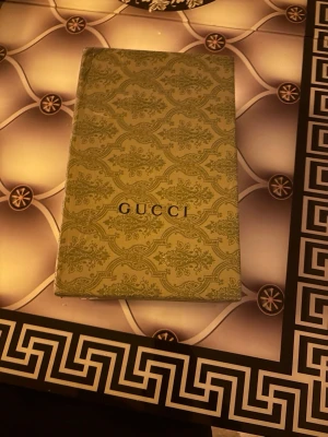 Gucci Ace sneakers med röd/blå detalj - Snygga Gucci Ace sneakers i svart med klassiskt GG-mönster, röda och blå ränder på sidan samt metallic-detaljer i rött och blått på hälen. Skorna har vita sulor och svarta skosnören. Perfekt för dig som vill sticka ut med lyxig streetstyle.