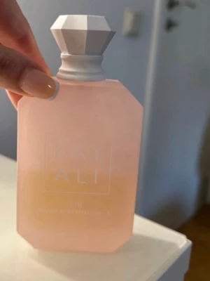 Kayali boujee marshmallow  - Säljer en elegant parfym från Kayali i en matt, ljusrosa flaska med geometrisk, vit kork. Flaskan har en modern, kantig form och känns lyxig och trendig. Perfekt för dig som gillar snygg design på parfymhyllan. Ca 40 ml kvar 