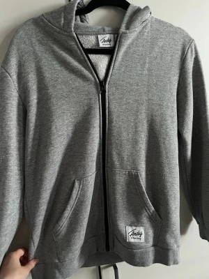 Grå zip hoodie  - Snygg grå hoodie med dragkedja från Andy by Frank Dandy i strl 150 (passar även tjej XS) Klassisk modell med huva, två stora fickor framtill och ribbade muddar. Tillverkad i mjukt sweatshirtmaterial som är borstat på insidan för extra komfort. Perfekt för vardagen. Sparsamt använd.