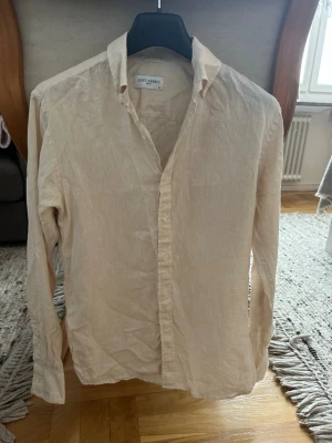 Beige linneskjorta från John Henric - Säljer en stilren beige skjorta från John Henric i svalt linne. Skjortan har klassisk krage, långa ärmar och knappar framtill. Perfekt för en avslappnad men ändå uppklädd look. Passar till både jeans och chinos.