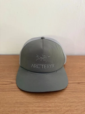 Grön/grå keps från Arc'teryx - Snygg sällsynt grön och grå keps från Arc'teryx med logga framtill. Justerbar snapback gör att den passar de vem som helst. Perfekt keps inför sommaren.