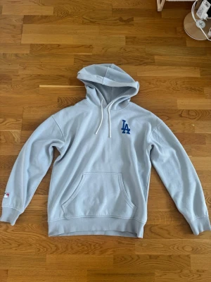 LA hoodie  - LA Hoodie – Storlek M (något större i passformen)  * Ljusblå hoodie med broderad LA-logga på bröstet. * Storlek M, men upplevs något större i storleken (mer åt en rymlig M eller mindre L). * Mjuk och bekväm kvalitet med skön insida. * Klassisk modell med huva, dragsnören och magficka framtill. * Ribbstickade muddar vid ärmslut och nederkant för bra passform. * Stilren färg som är lätt att matcha med jeans, shorts eller mjukisbyxor. * Fint skick utan anmärkningar. * Perfekt för både vardag och av