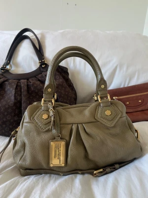 Khaki grön Q Classic Baby Groove bag! - Så fin khaki grön handväska i äkta läder från Marc by Marc Jacobs. Den ikoniska modellen Q Classic Baby Groove! En populär och eftertraktad vintagemodell med gulddetaljer och dubbla handtag. Långa bandet medföljer. Så snygg vintageväska i toppskick, inga skavanker. Ren invändigt och fina gulddetaljer. Svår att få tag på i detta skick. Skriv privat för fler bilder 🤍  Mått: Lilla modellen. 34x18x12 cm (undersida)  Kan hämtas hemma hos mig i Nacka eller skickas 🤍 