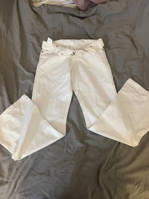 Vita bootcut jeans med låg midja - Säljer ett par vita bootcut jeans med låg midja och dekorativa knappar framtill. Jeansen har en utsvängd passform från knät och är tillverkade i ett klassiskt denimtyg. Perfekta jeansen helt enkelt! Aldrig använt dessutom 