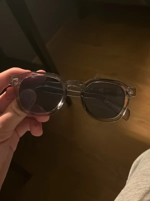 Runda transparenta solglasögon  - Snygga solglasögon med rund form och transparent plastbåge. Glasen är mörka och ger en cool kontrast till den klara ramen. Perfekta för att lyfta din stil under soliga dagar.