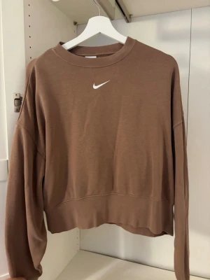 Brun croppad sweatshirt från Nike - Säljer en brun croppad sweatshirt från Nike med klassisk vit logga broderad på bröstet. Tröjan har rund halsringning och långa ärmar. Ca 500 kr nypris. 