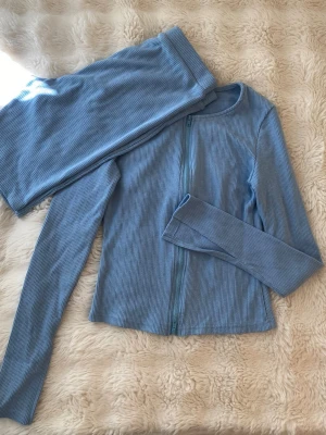 Blått set - Babyblå set, shorts och tröja med slits i armarna och dragkedja.