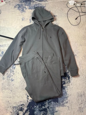 Mörkgrå Ralph Lauren tracksuit  - Säljer en riktigt snygg Mörkgrå Polo tracksuit i en snygg mörkgrå färg. Storlek M på hoodien och L på byxorna. Äkta
