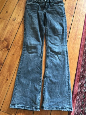 Blå bootcut jeans med fickdetaljer - Säljer ett par klassiska blå bootcut jeans med snygga fickdetaljer bak och knappstängning. Jeansen har en avslappnad passform med utsvängda ben och är tillverkade i mjukt denimtyg. 